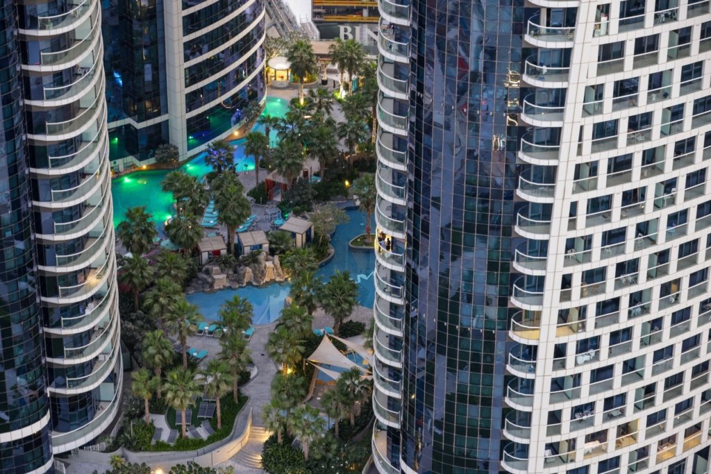 Aerial view of high-rise Dubai residential towers with landscaped pool and palm trees, representing overseas-owned rental property