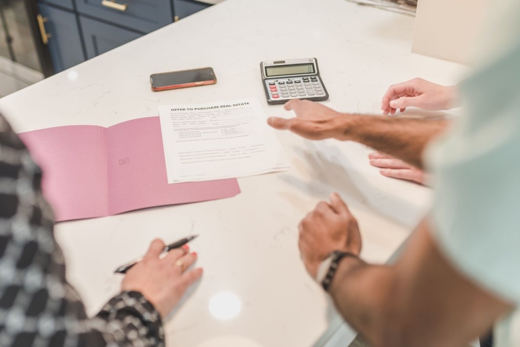 Real estate buyer signing an offer to purchase real estate form next to a calculator and phone, representing Dubai property buying costs