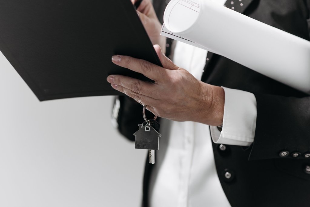 Real estate agent in a suit holding property documents and a house-shaped key ring, representing property title and ownership transfer