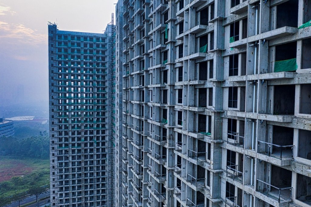 Unfinished high-rise residential towers under construction with visible concrete frame and green safety netting, representing a delayed off-plan project in Dubai