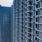 Unfinished high-rise residential towers under construction with visible concrete frame and green safety netting, representing a delayed off-plan project in Dubai