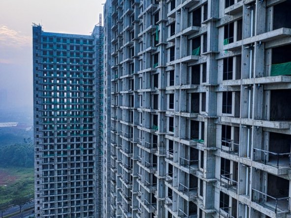 Unfinished high-rise residential towers under construction with visible concrete frame and green safety netting, representing a delayed off-plan project in Dubai
