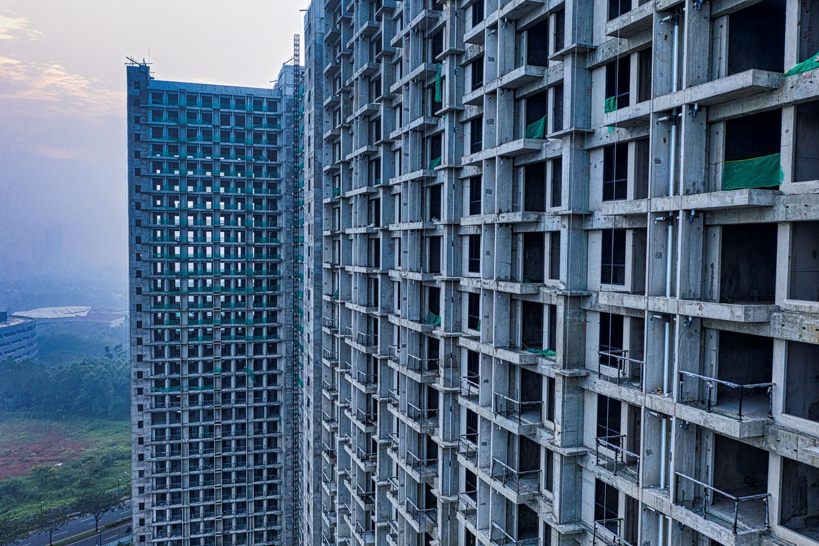 Unfinished high-rise residential towers under construction with visible concrete frame and green safety netting, representing a delayed off-plan project in Dubai