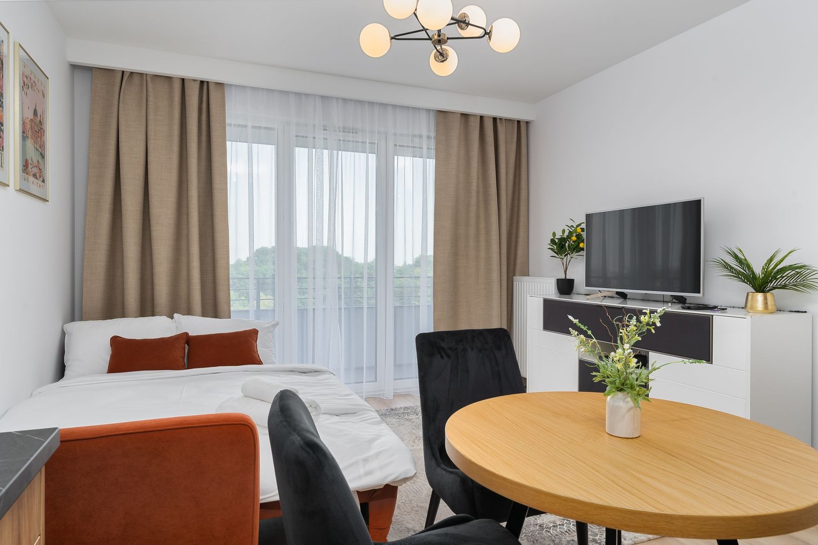 Bright modern studio apartment interior with a sofa bed, round dining table, TV and balcony doors