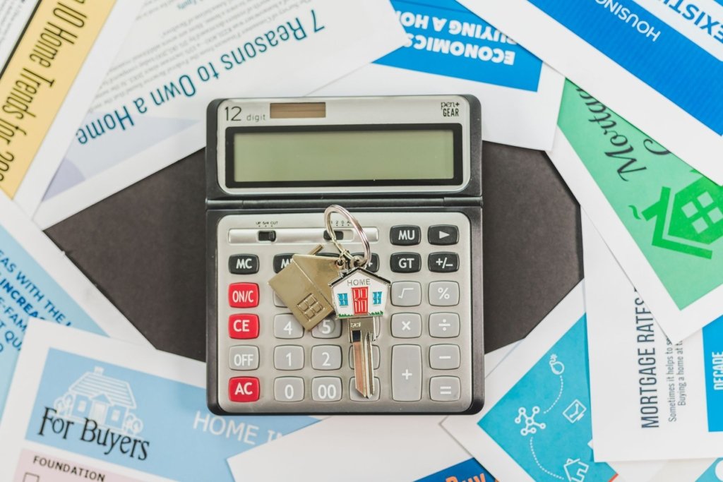 Calculator with a home-shaped key on top, surrounded by real estate and mortgage information flyers