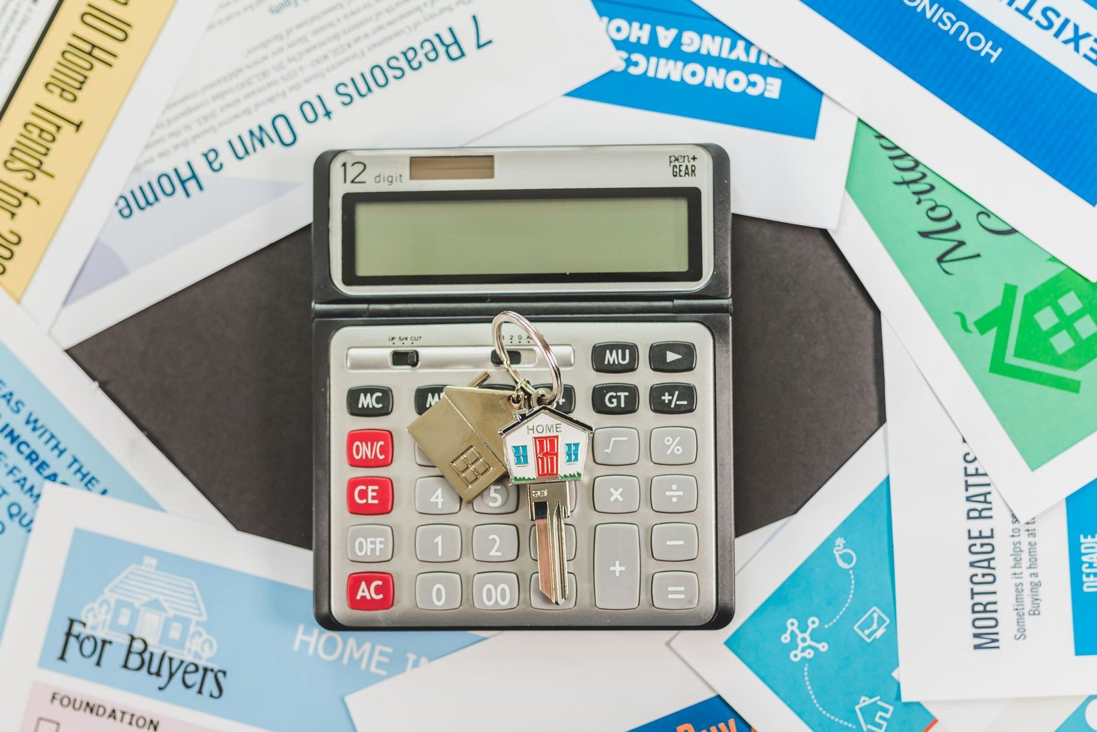 Calculator with a home-shaped key on top, surrounded by real estate and mortgage information flyers