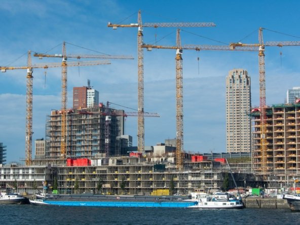 Tower cranes over a residential building site on a waterfront, with a cargo barge moored in the foreground