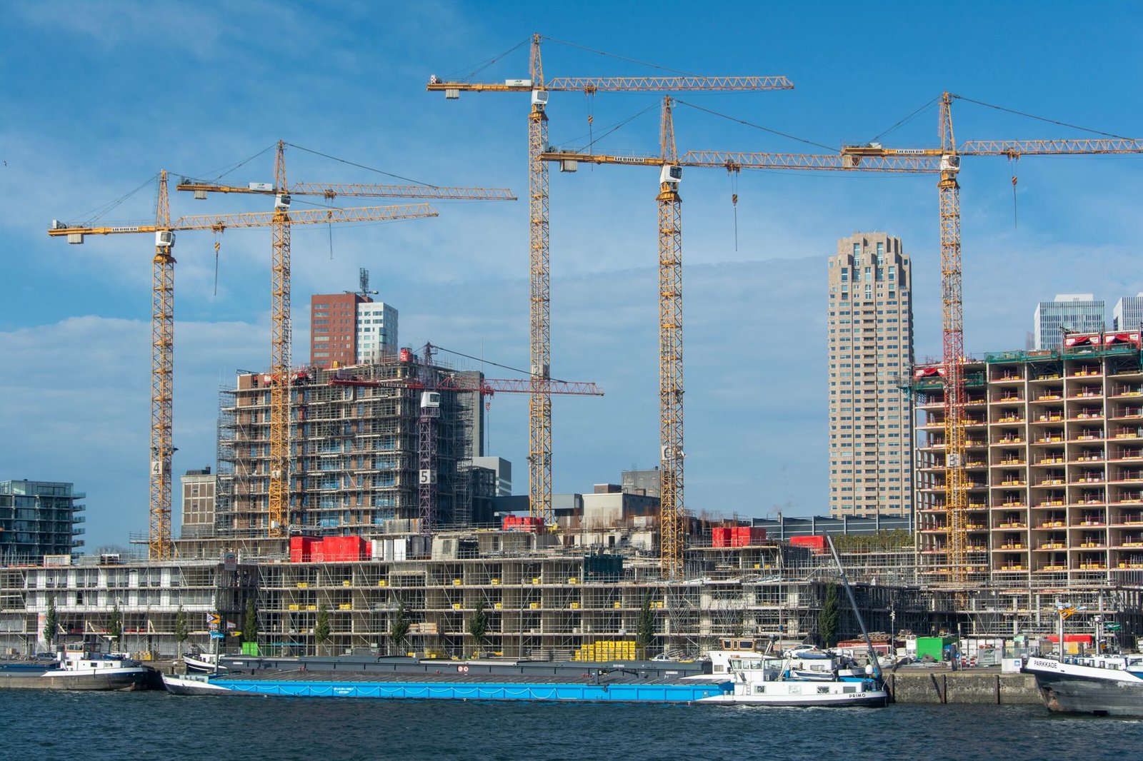 Tower cranes over a residential building site on a waterfront, with a cargo barge moored in the foreground