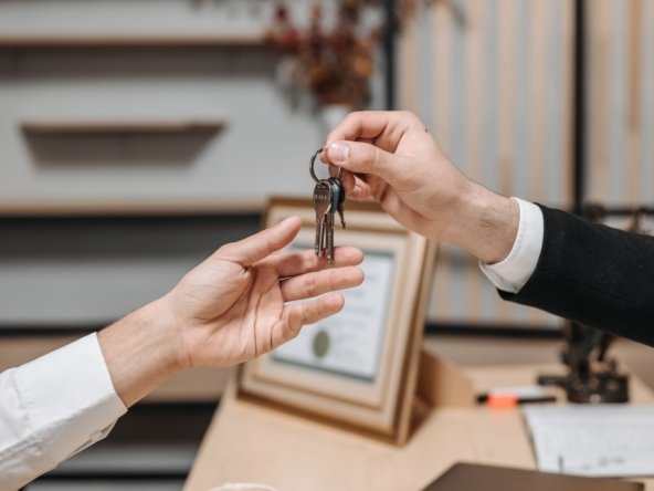 Close-up of one hand handing a set of keys to another hand across a desk, illustrating a landlord and tenant key handover