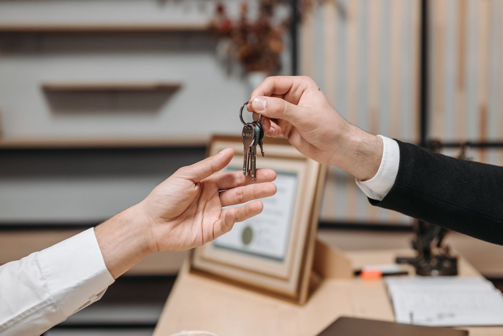 Close-up of one hand handing a set of keys to another hand across a desk, illustrating a landlord and tenant key handover