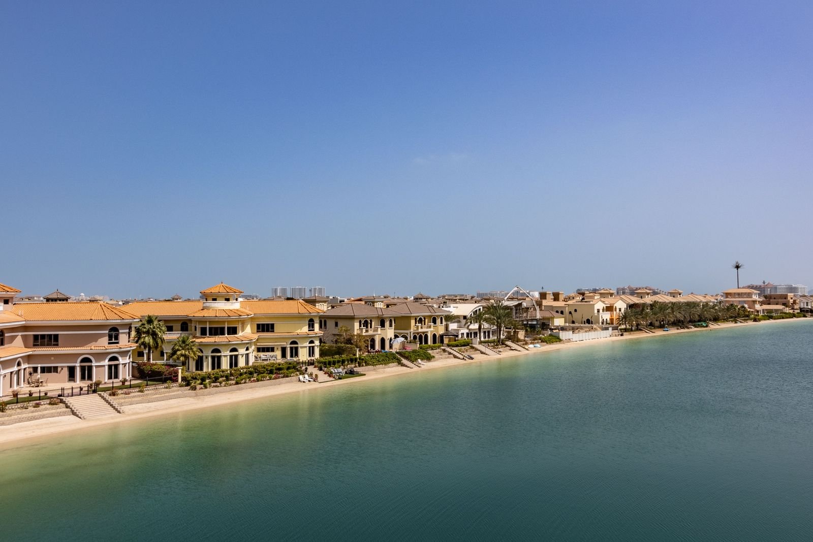 Mediterranean-style waterfront villas with terracotta roofs beside calm turquoise water in Dubai