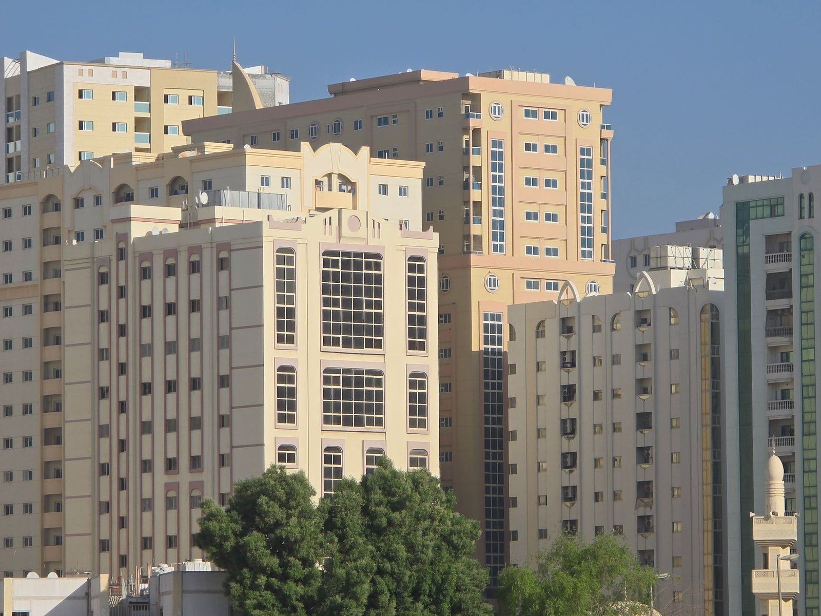 Cream and beige apartment buildings with trees under a clear blue sky