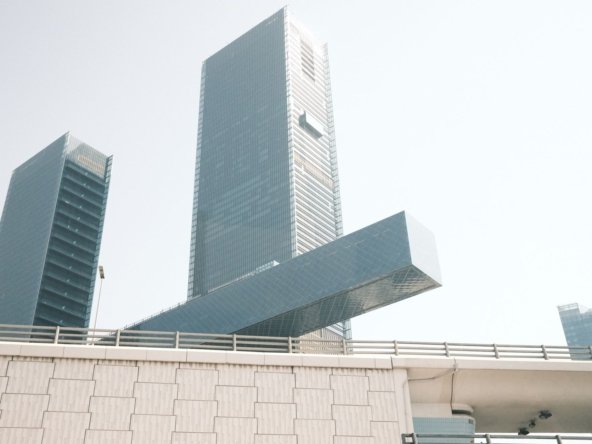 Glass office towers with a cantilevered glass section rising above a highway overpass in Dubai