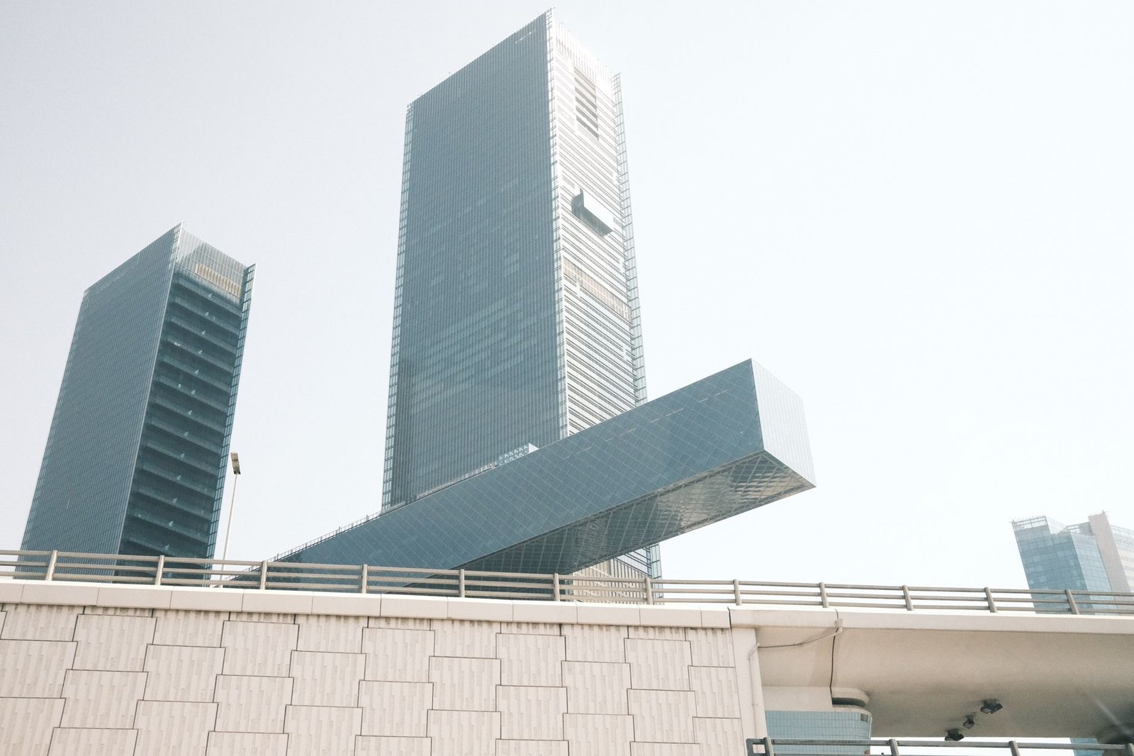 Glass office towers with a cantilevered glass section rising above a highway overpass in Dubai