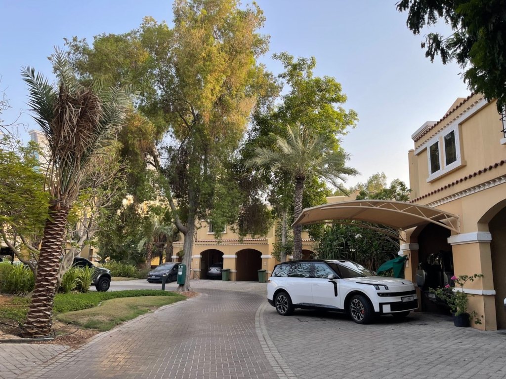 Row of Spanish-style townhouses with a shaded driveway, palm trees and carports in a Dubai villa community