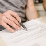 Close-up of a hand holding a pen over a printed contract, illustrating reading the lease and notice terms before buying or selling a tenanted property