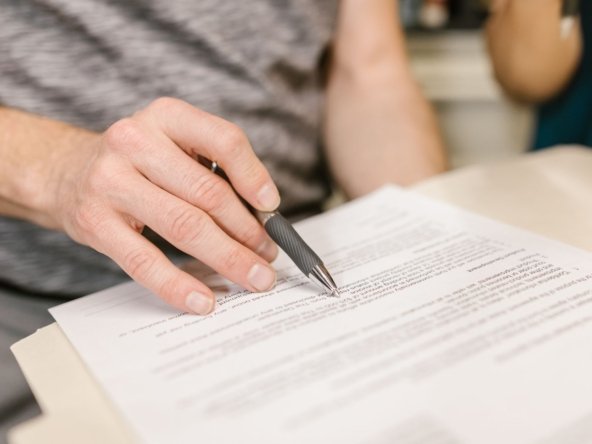 Close-up of a hand holding a pen over a printed contract, illustrating reading the lease and notice terms before buying or selling a tenanted property