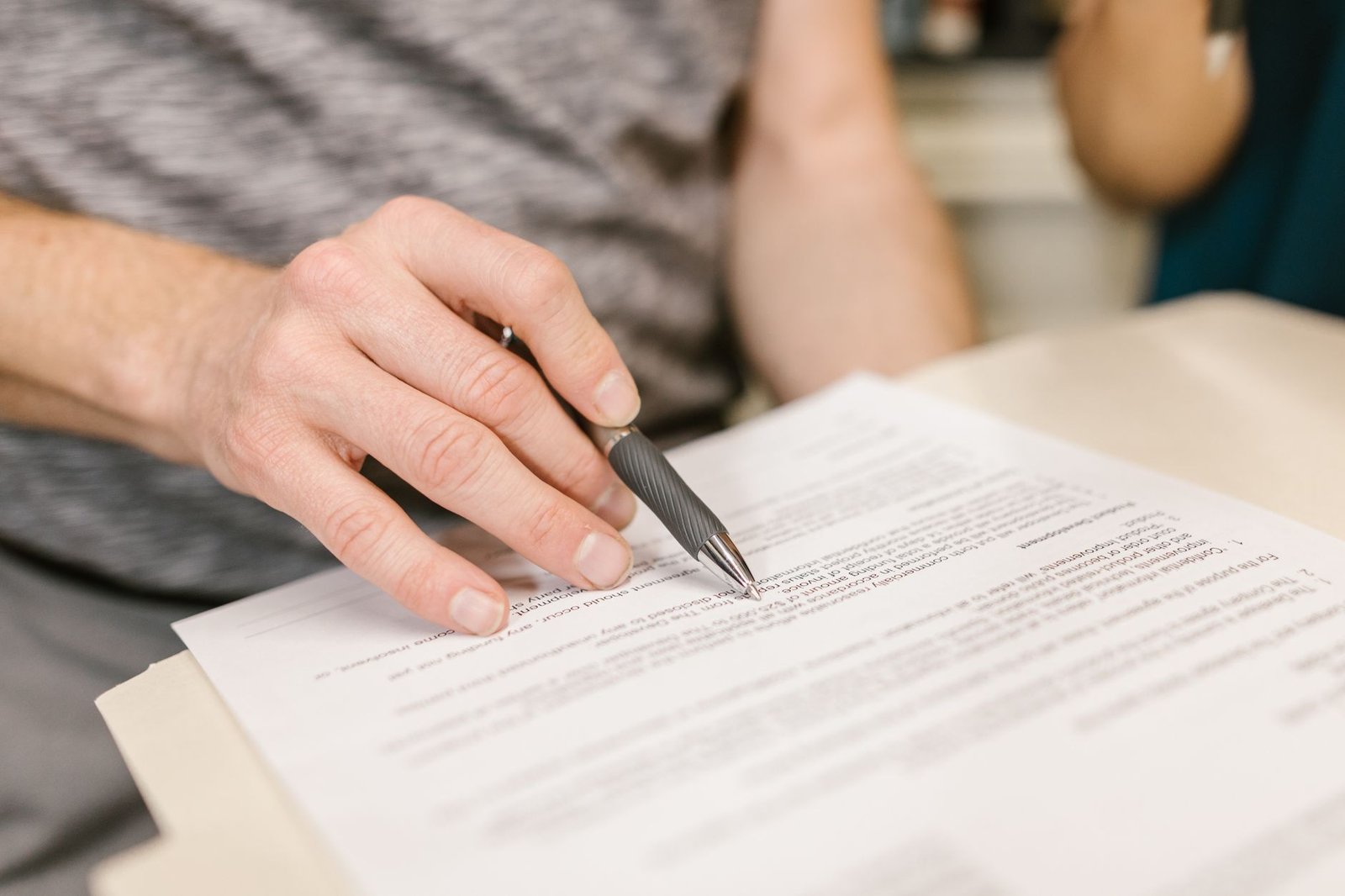 Close-up of a hand holding a pen over a printed contract, illustrating reading the lease and notice terms before buying or selling a tenanted property