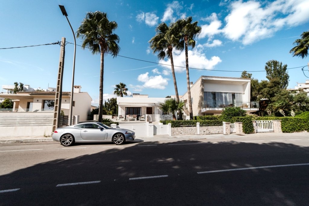 Row of detached white villas with palm trees under a blue sky, illustrating a gated villa community like The Meadows Dubai