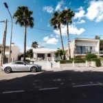 Row of detached white villas with palm trees under a blue sky, illustrating a gated villa community like The Meadows Dubai