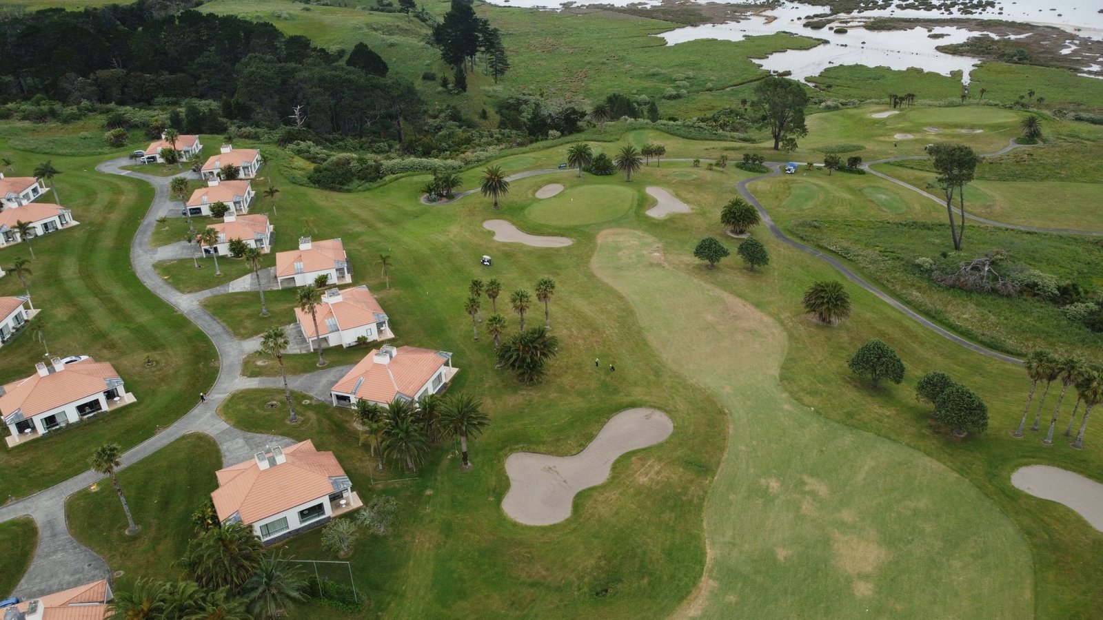 Aerial view of villas with terracotta roofs lining a golf course fairway with palm trees and sand bunkers