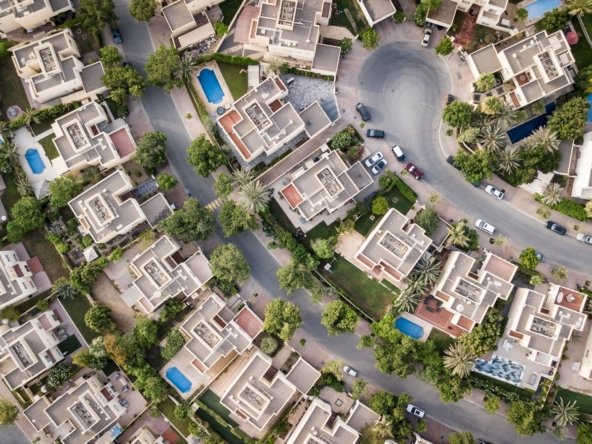 Aerial photograph of villa and townhouse rooftops with pools in a gated Dubai community