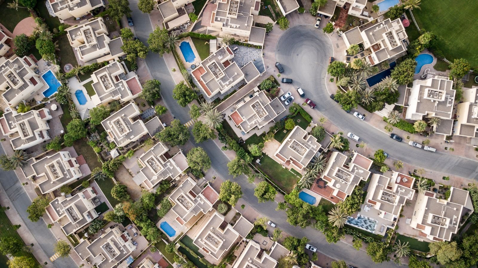 Aerial photograph of villa and townhouse rooftops with pools in a gated Dubai community