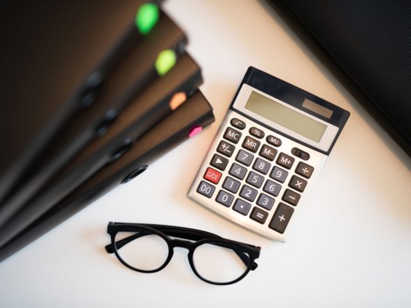 Overhead view of a calculator and reading glasses beside stacked document folders on an office desk, illustrating preparing a tax return for overseas property
