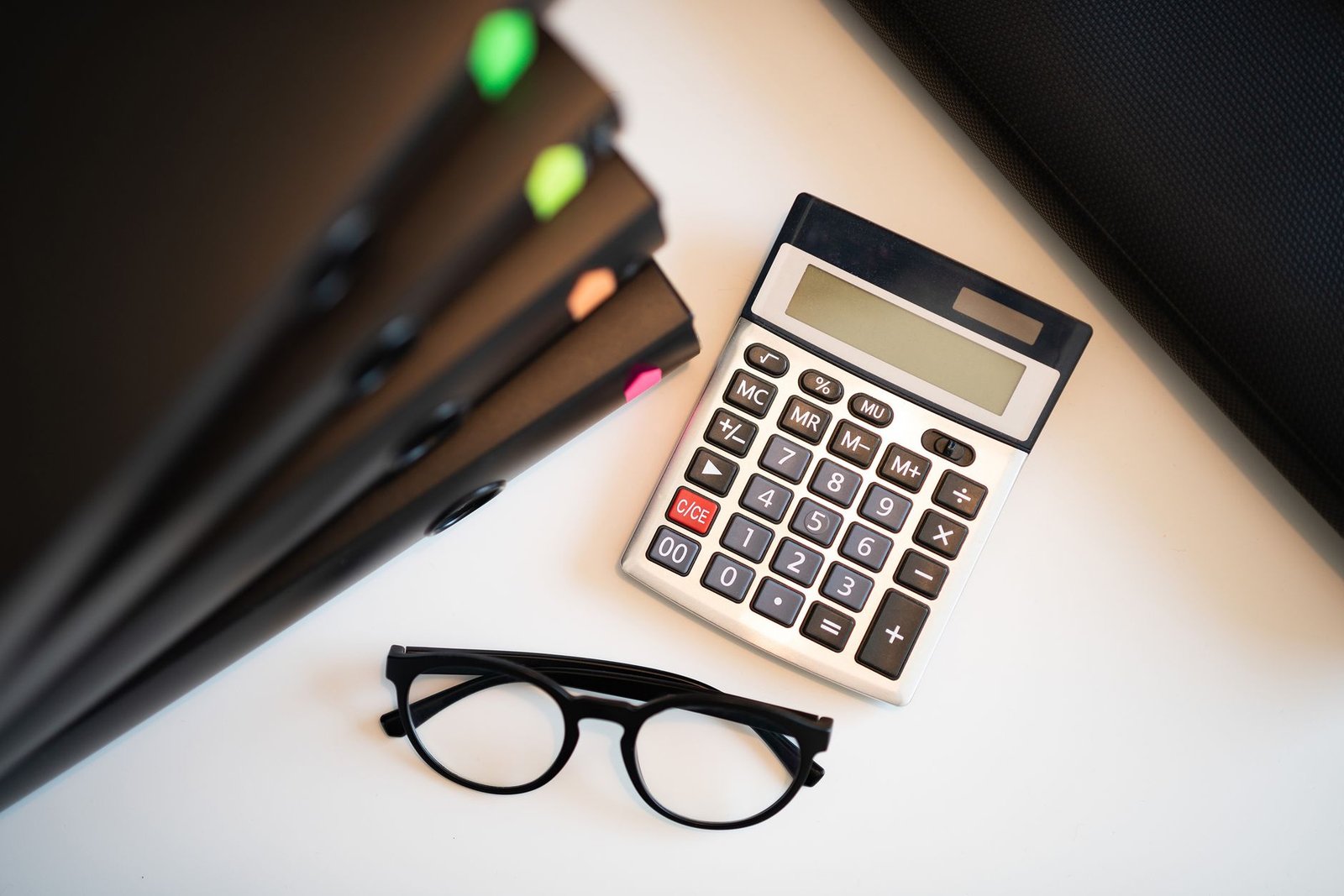 Overhead view of a calculator and reading glasses beside stacked document folders on an office desk, illustrating preparing a tax return for overseas property