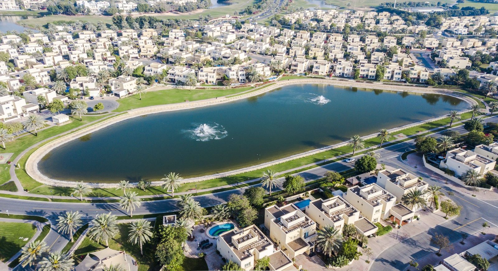 Aerial view of villas around a lake with fountains in a Dubai suburban community
