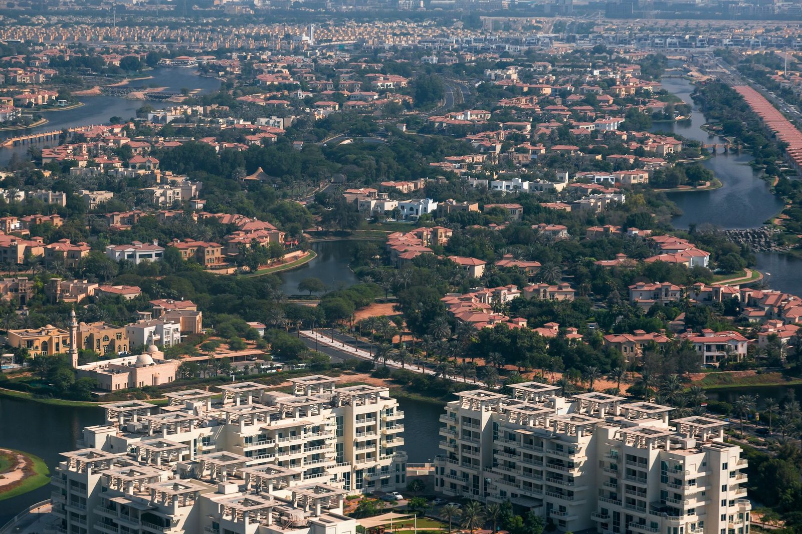 Aerial view of terracotta-roofed villas and apartment blocks beside lakes and palm-lined roads