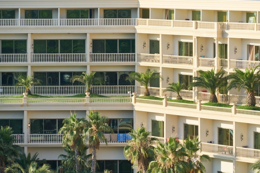 Low-rise apartment building with balconies and palm trees, representing The Greens apartment community in Dubai