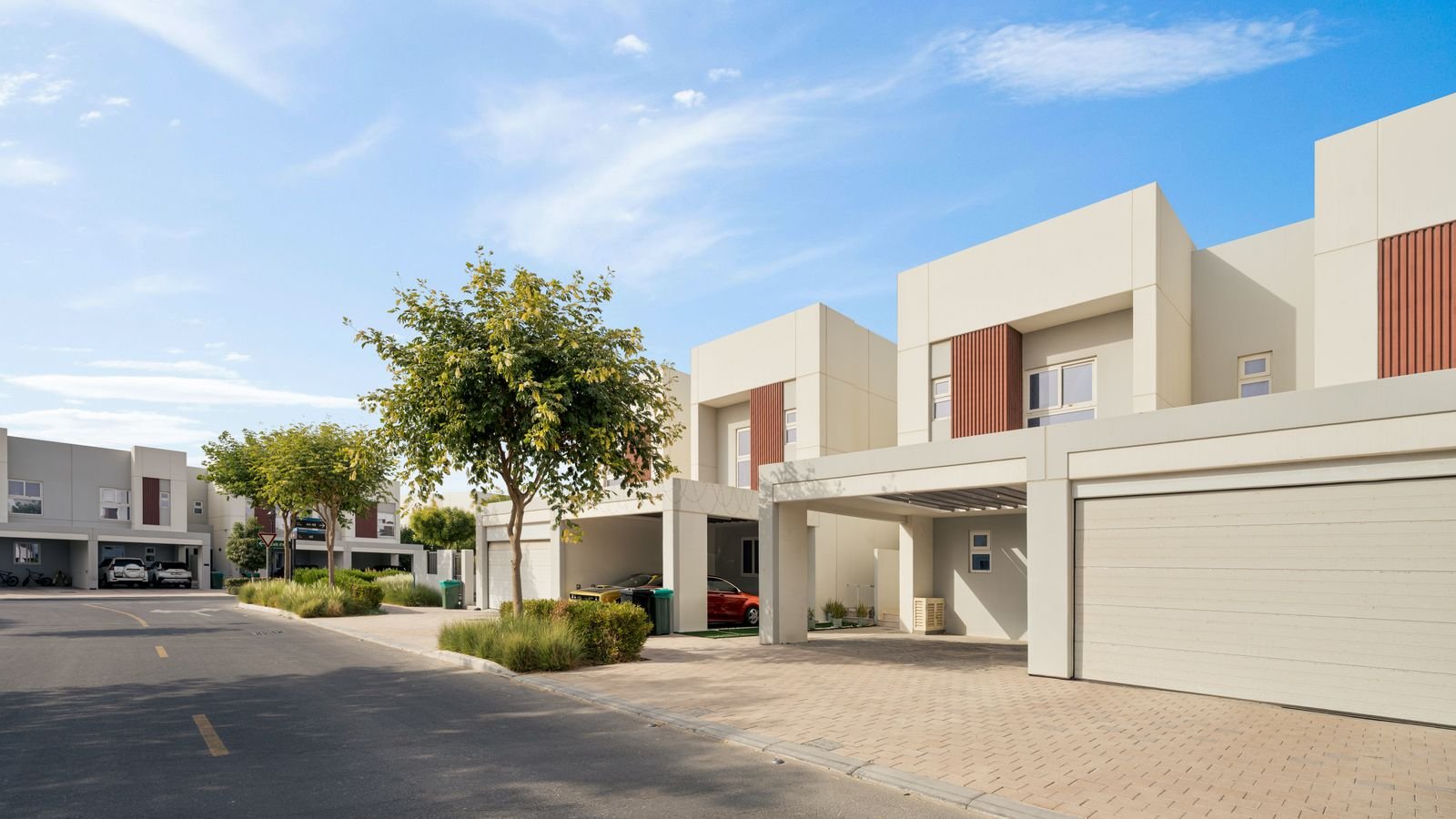 Row of modern two-storey townhouses with landscaped street under blue sky in a Dubai residential community